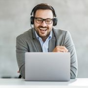 Happy male entrepreneur with headphones talking to someone during conference call over a computer in the office. Copy space.